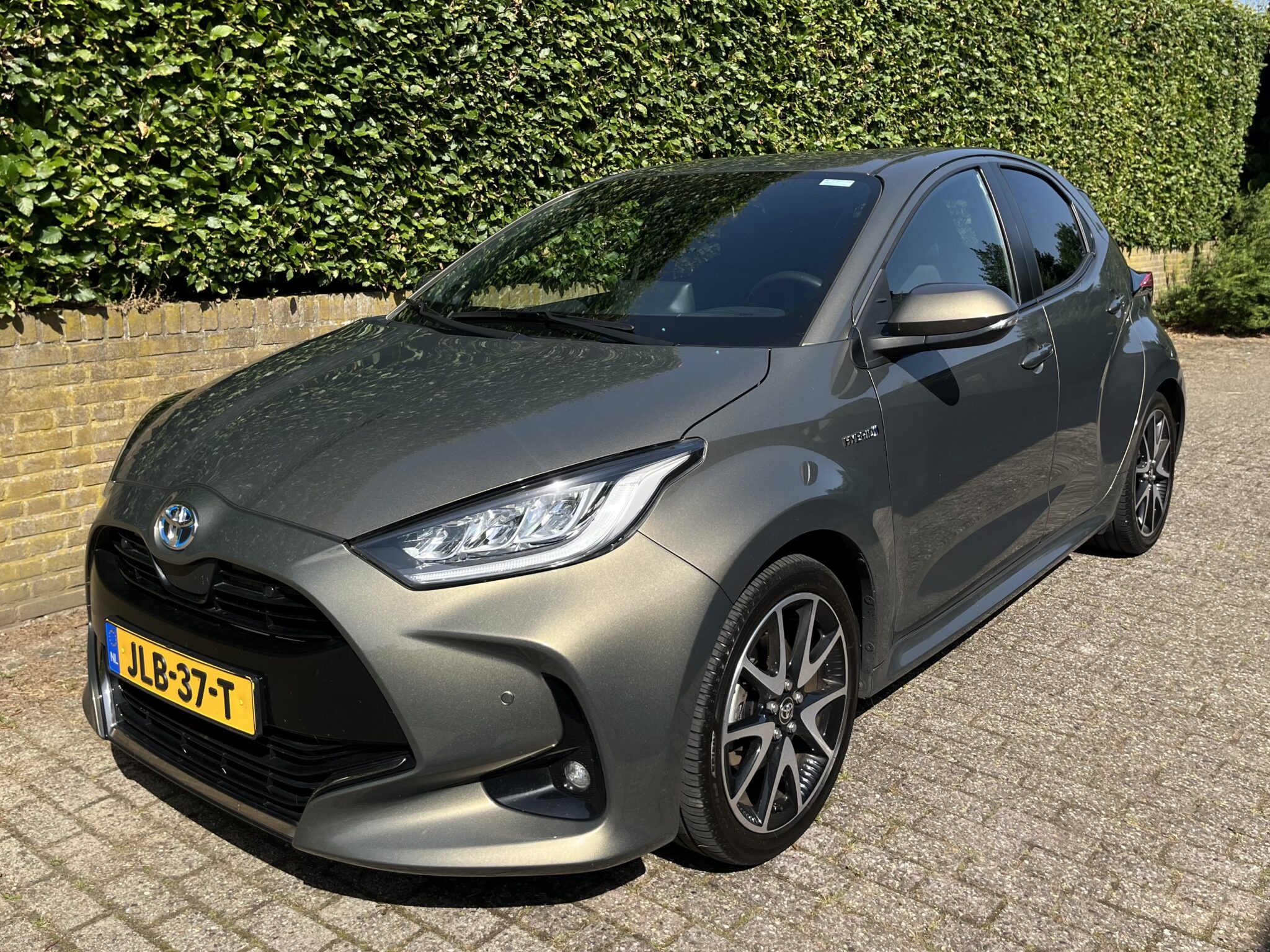 Toyota Yaris 1.5 Hybrid Executive, een auto uit 2021 in de kleur groen metallic, driekwart vooraanzicht op de klinkerbestrating bij Entink Automotive